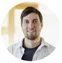 Ein Mann mit kurzen braunen Haaren und Bart lächelt in die Kamera. Er trägt ein weißes Hemd mit Fahrrad-Design auf der linken Brust.