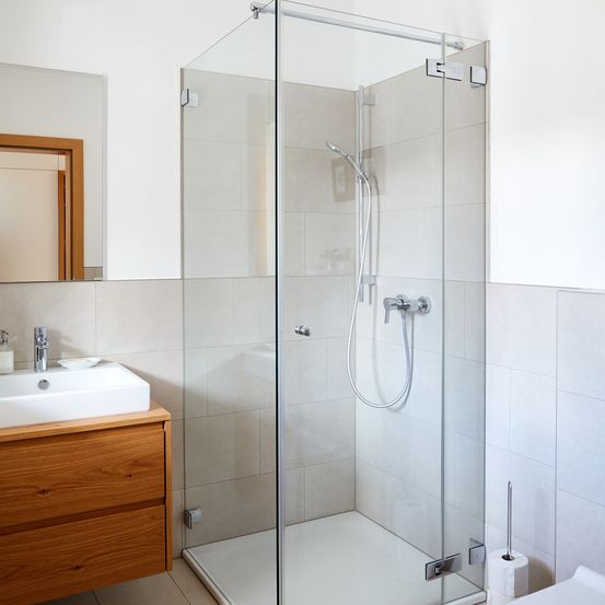 Ein Badezimmer mit einer gläsernen Duschkabine, einem weißen Waschbecken, einem hölzernen Schrank und einem Spiegel mit hölzerne Rahmen.