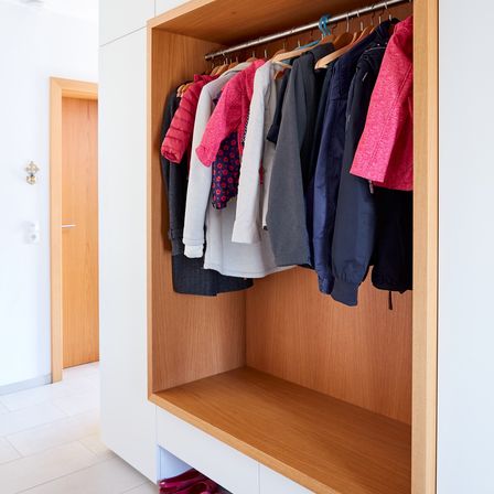 Eine Nahaufnahme eines Holzschranks mit verschiedenen farbigen Kleidern, die hängen, und einer Bank darunter mit Schuhen.