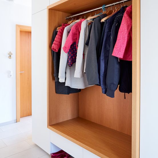 Eine Nahaufnahme eines Holzschranks mit verschiedenen farbigen Kleidern, die hängen, und einer Bank darunter mit Schuhen.