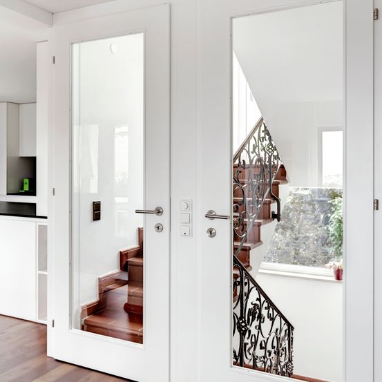 Ein Innenansicht zeigt eine weiße Tür mit Glasscheiben, die eine Wendeltreppe und ein Fenster mit einem Topfpflanzen reflektiert.