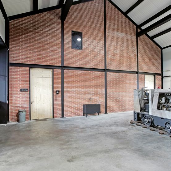 Ein leerer Raum mit einer Ziegelwand, einer Holztür, einem Mülleimer und einer großen Maschine auf einem Palette.