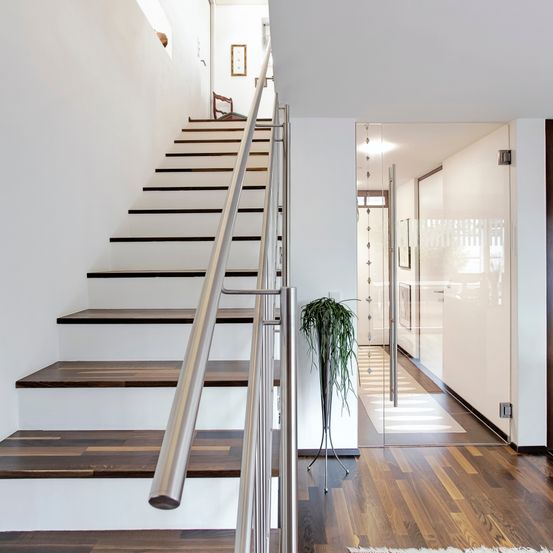 Modernes Interieur eines Hauses mit weißer Wand und Holzboden. Es gibt eine weiße Treppe mit metallenem Handlauf.