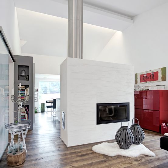 Ein modernes Wohnzimmer mit weißen Wänden, einem Kamin und einem roten Schrank. Ein weißer Fellteppich und zwei Laternen stehen auf dem Boden. Eine Bücherregal mit Büchern und einem Kerzenständer ist in der Ecke.