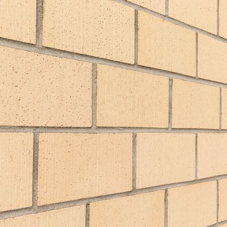 Eine Nahaufnahme einer beigen Ziegelmauer mit Zementfugen. Die Ziegelsteine haben eine einheitliche Textur und Farbe.