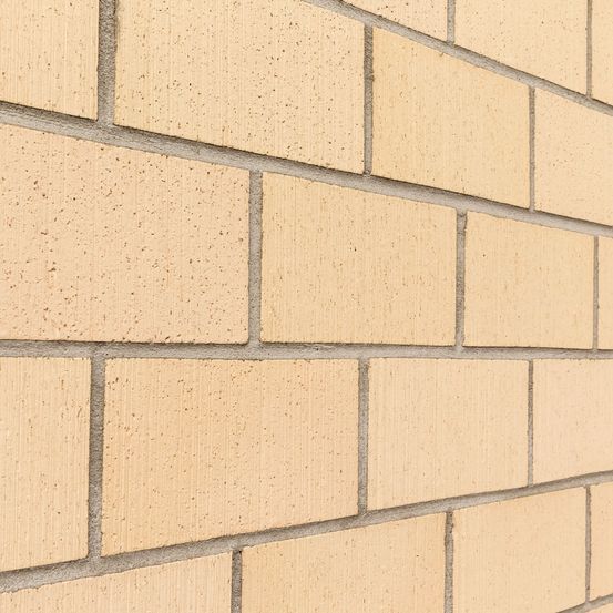 Eine Nahaufnahme einer beigen Ziegelmauer mit Zementfugen. Die Ziegelsteine haben eine einheitliche Textur und Farbe.