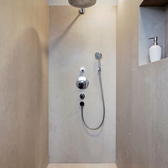 Ein Duschbereich mit Duschkopf, Seifenspender und grauen Betonwänden.