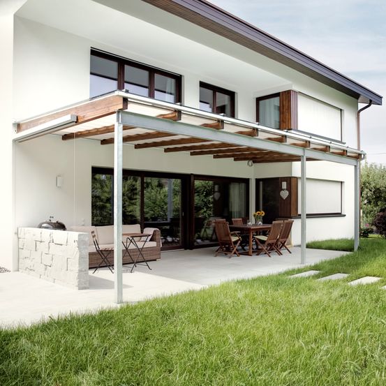 Ein modernes weißes Haus mit einer Terrasse, die eine Metallpergola, Außensitzplätze und einen Essbereich mit Tisch und Stühlen bietet.