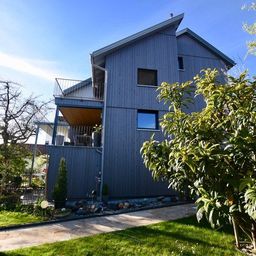 Ein modernes Haus mit blauer Außenseite, einem Balkon und einem grünen Rasen davor.