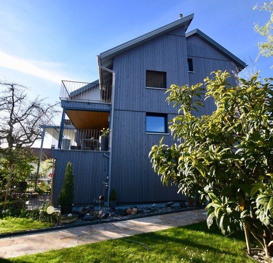 Ein modernes Haus mit blauer Außenseite, einem Balkon und einem grünen Rasen davor.