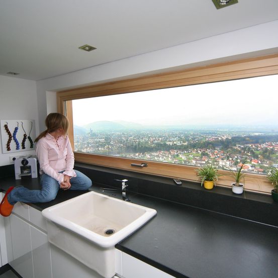 Eine Frau sitzt auf einer Küchentheke mit Blick auf eine Stadt und Berge draußen.