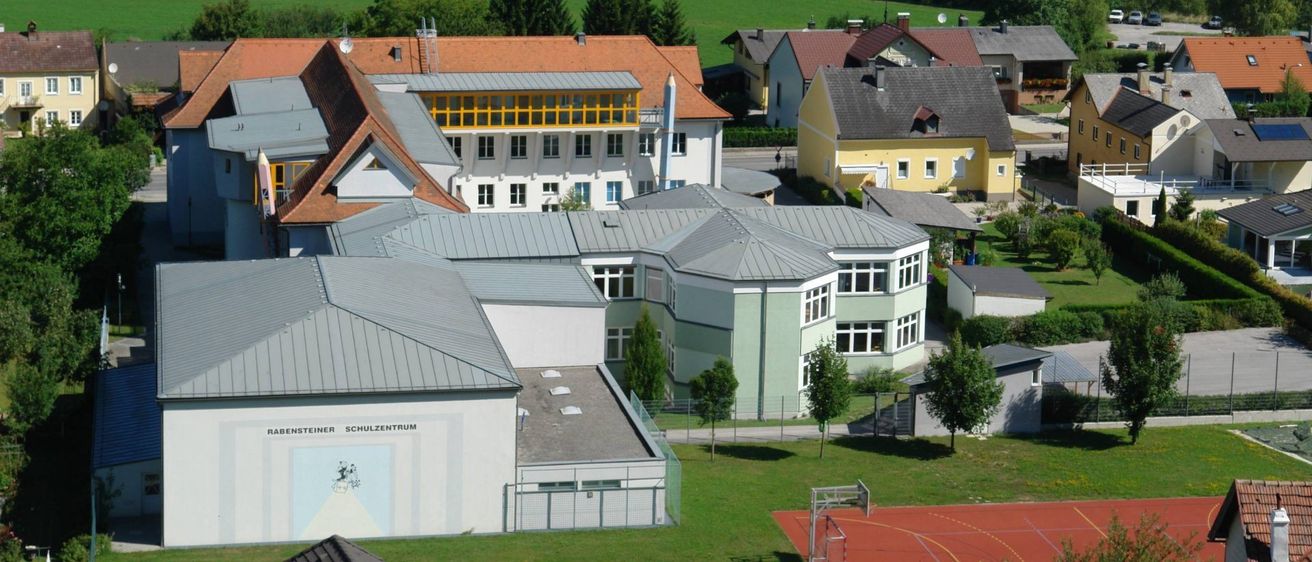 Ein Luftbild einer Schule mit mehreren Gebäuden, einem Basketballplatz und umgeben von Bäumen und Gras.