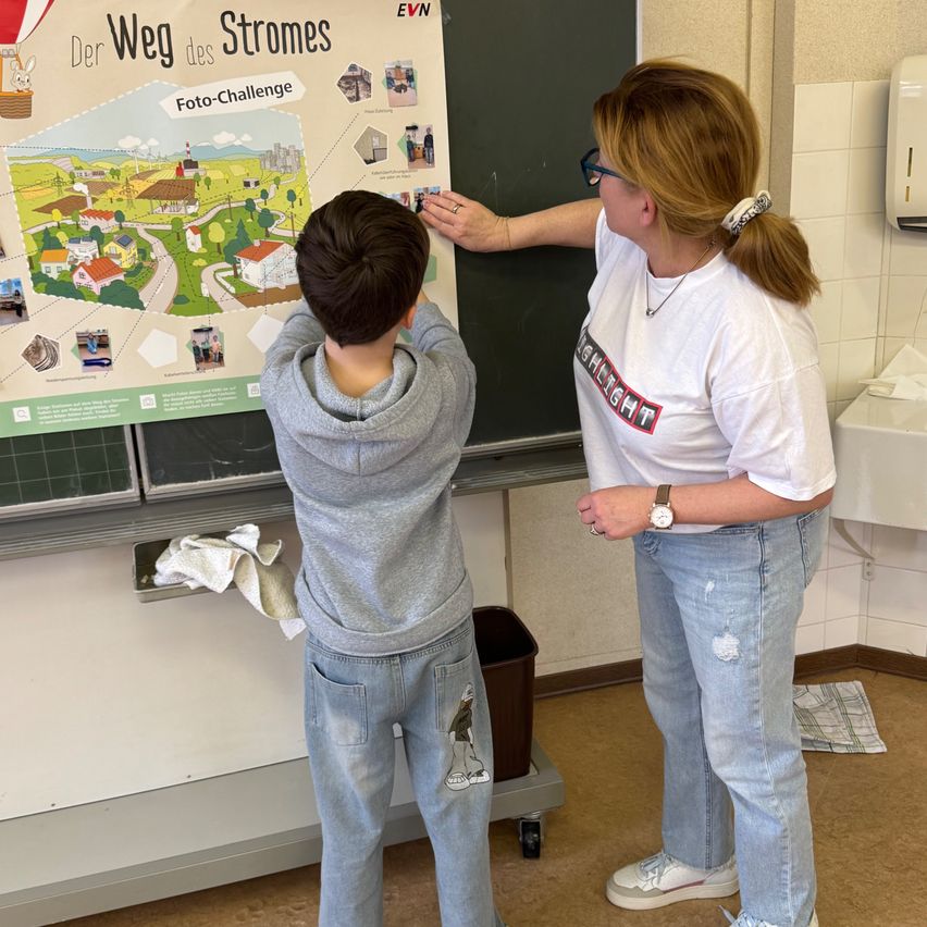 Eine Frau und ein Junge stehen vor einer Tafel mit einer Karte mit dem Titel 'Der Weg des Stromes'. Der Junge berührt die Tafel, während die Frau darauf zeigt.