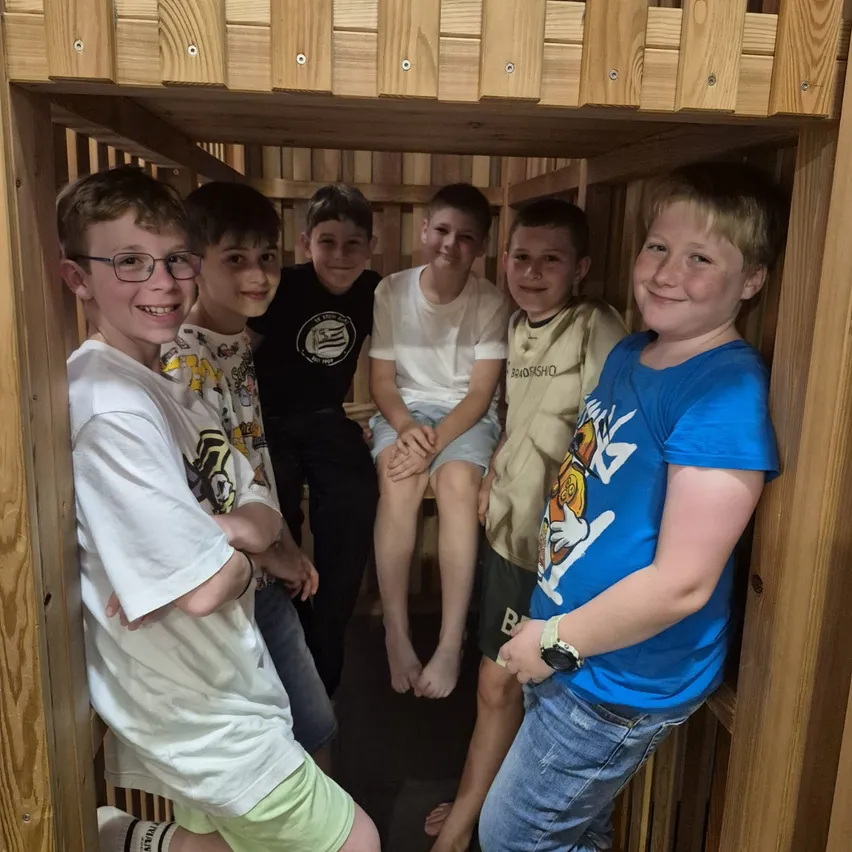 Eine Gruppe junger Jungen steht in einem Holzspielhaus, lächelt und posiert für ein Foto. Ein Junge sitzt auf einem Etagenbett.