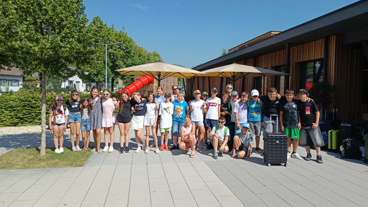 Eine Gruppe von Kindern und Teenagern posiert für ein Foto vor einem Gebäude mit Bäumen und Schirmen im Hintergrund.