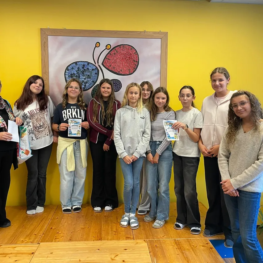 Eine Gruppe junger Mädchen und Frauen posiert für ein Foto vor einer gelben Wand mit einem Schmetterlingsbild.