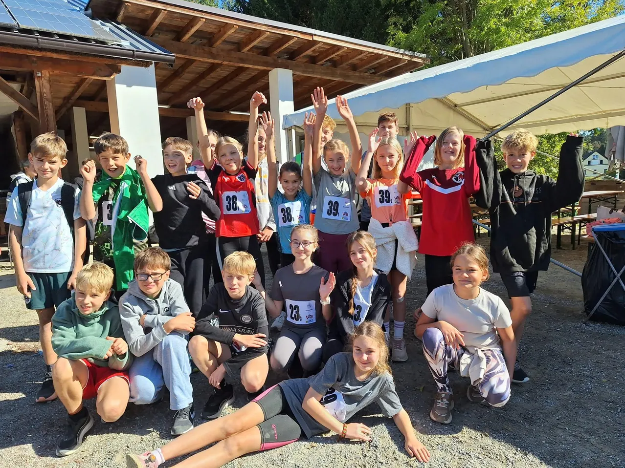 Eine Gruppe von Kindern mit nummerierten Startnummern posiert für ein Foto vor einem Gebäude.