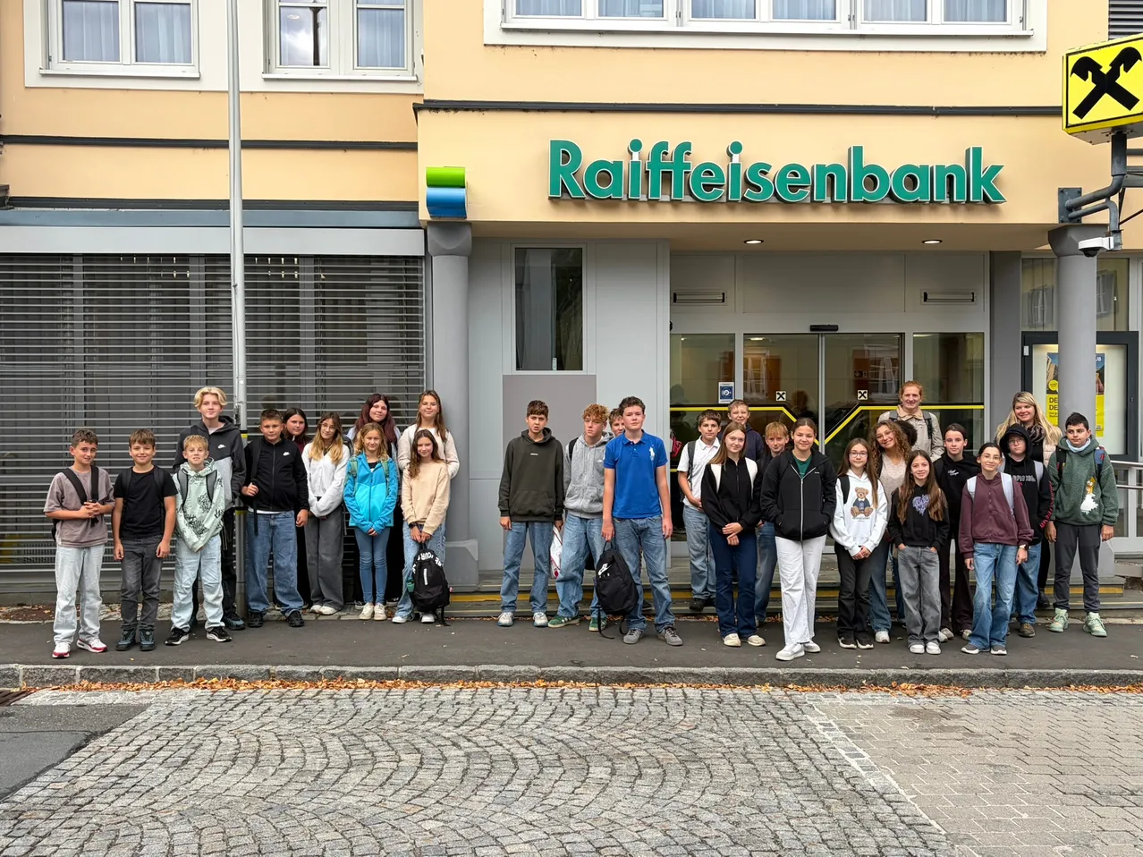 Eine Gruppe von Schülern steht vor einem Raiffeisenbank-Gebäude und lächelt für ein Gruppenfoto.