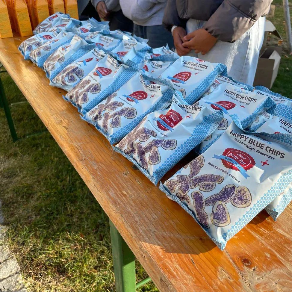Ein Holztisch mit mehreren Tüten Happy Blue Chips, einem Snack-Lebensmittel, darauf ausgestellt.