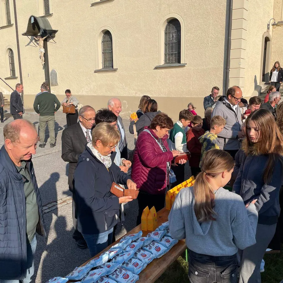 Eine Gruppe von Menschen versammelt sich vor einer Kirche, einige erhalten Essen von einem Tisch.