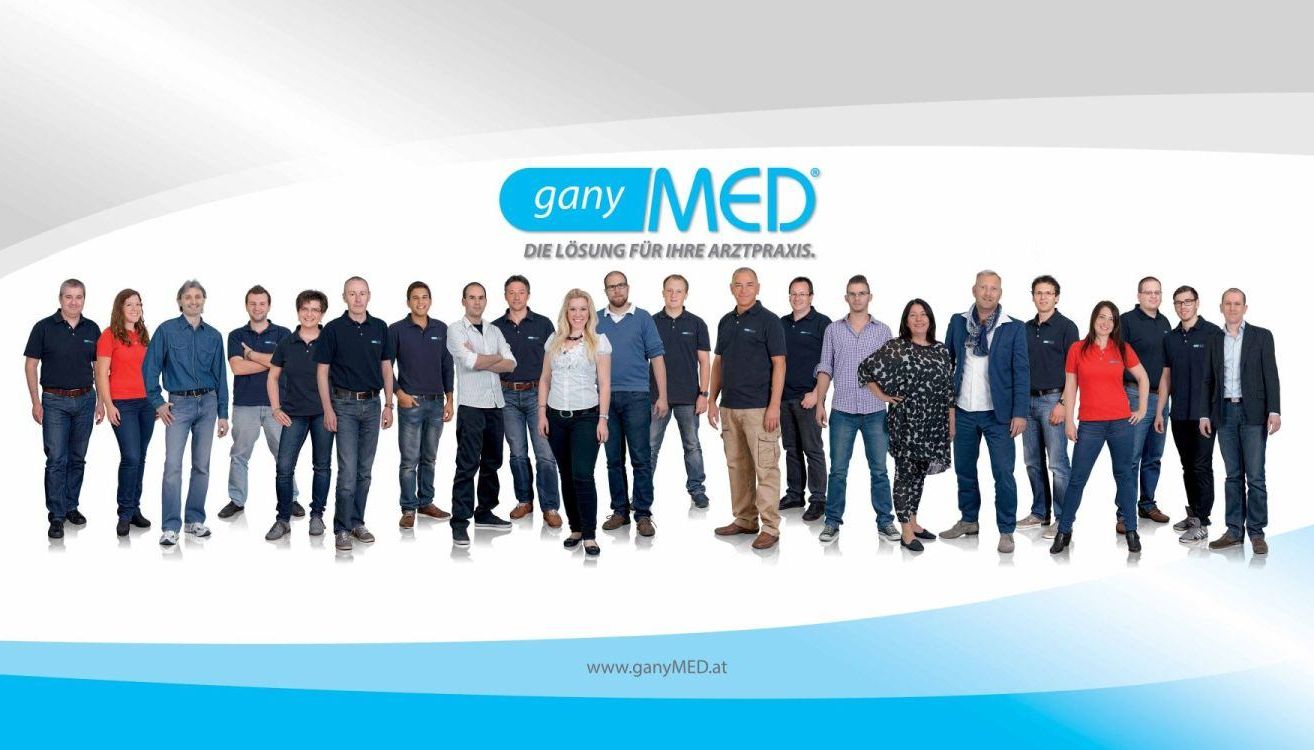 Eine Gruppe von Menschen, die in Blau und Weiß gekleidet sind, steht in einer Reihe für ein Foto. Das Logo 'ganyMED' ist oben sichtbar.