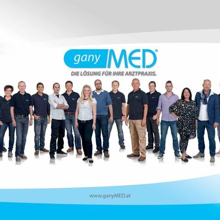 Eine Gruppe von Menschen, die in Blau und Weiß gekleidet sind, steht in einer Reihe für ein Foto. Das Logo 'ganyMED' ist oben sichtbar.