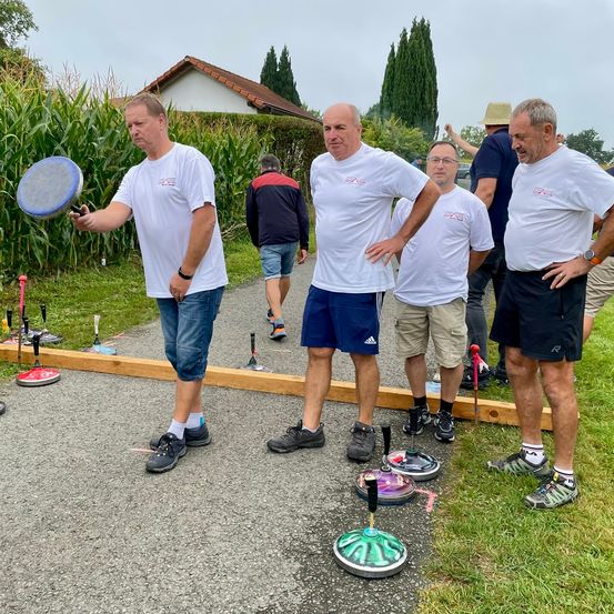 Eine Gruppe von Männern in weißen T-Shirts und Turnschuhen spielt draußen an einem sonnigen Tag eine Partie Boccia.