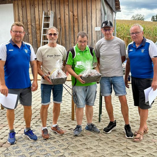 Fünf Männer stehen in einer Reihe und halten Geschenkkörbe, mit einem Holzgebäude und Maisfeld im Hintergrund.