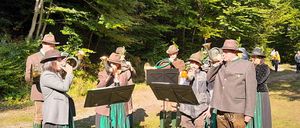 Eine Gruppe von Menschen in traditionellen Kostümen steht in einem Wald und spielt Blechblasinstrumente.
