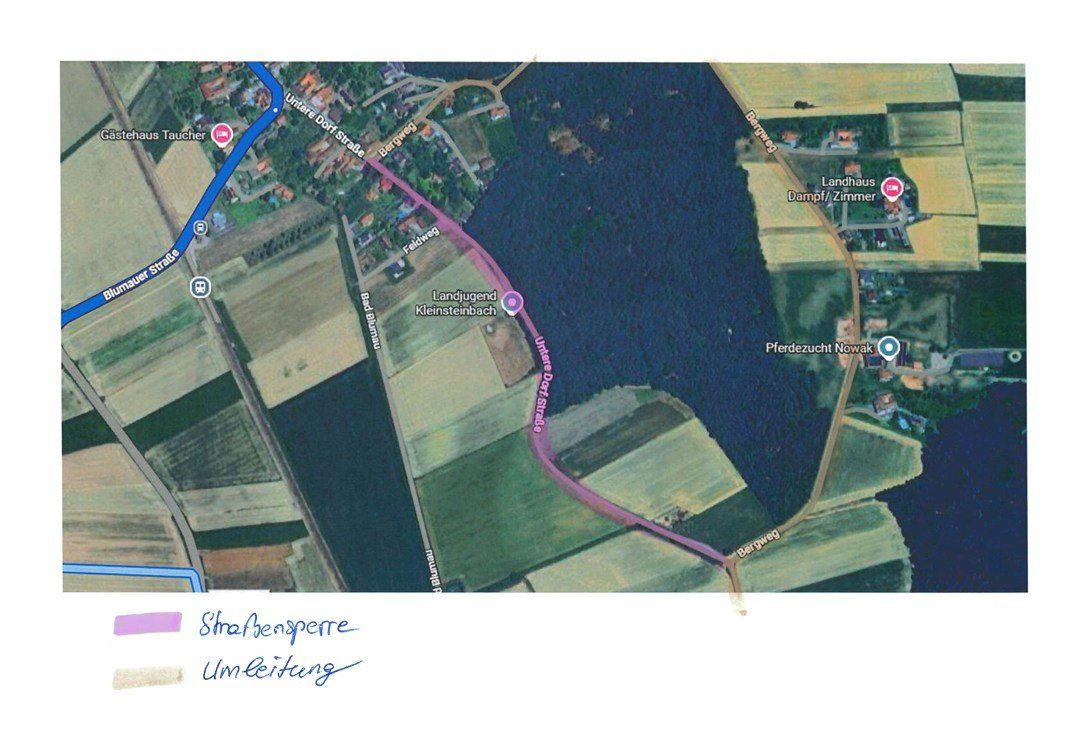 Luftaufnahme eines Flusses mit einer Straße auf der linken Seite. Eine blaue Linie markiert einen Weg, und eine rosa Linie markiert eine andere Route. Gebäude und Grünflächen sind verstreut.