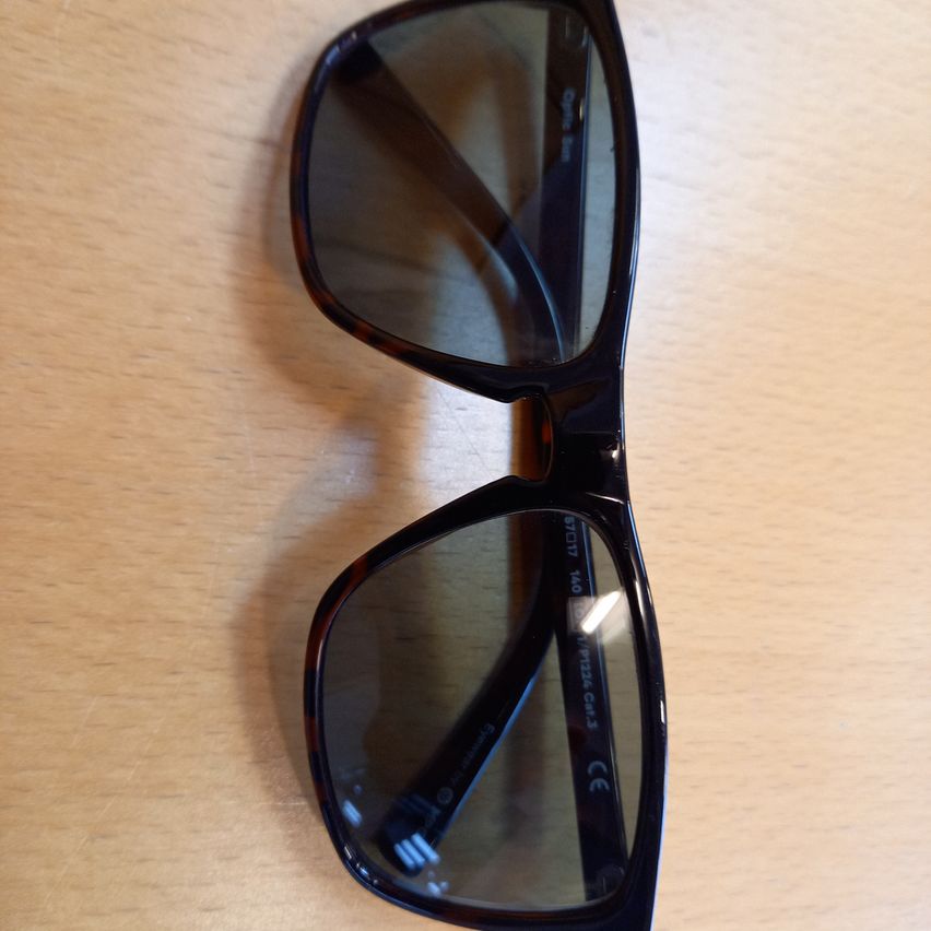 A pair of black sunglasses with rectangular lenses and brown frames, placed on a wooden surface.