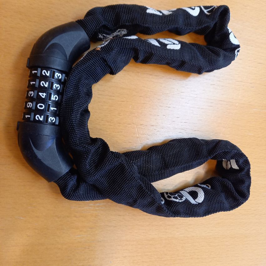 A black bicycle lock with a combination lock is placed on a wooden surface. The lock features a combination dial with numbers 1 through 9 and a lock mechanism.