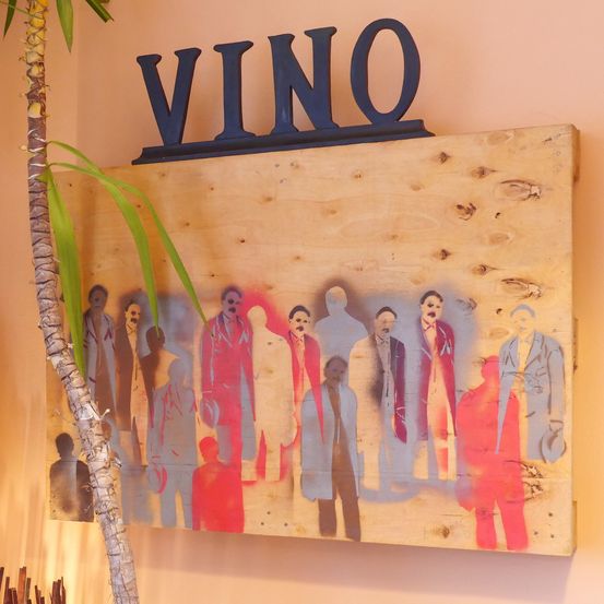 Ein Holzschild mit dem Wort 'VINO' darauf zeigt ein Gemälde von Männern in Anzügen, die in einer Reihe stehen.