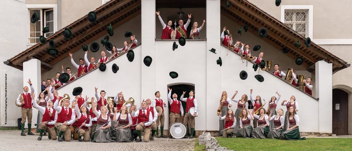 Eine Gruppe von Musikern in traditioneller Kleidung, die ihre Hüte vor einem Gebäude in die Luft werfen.