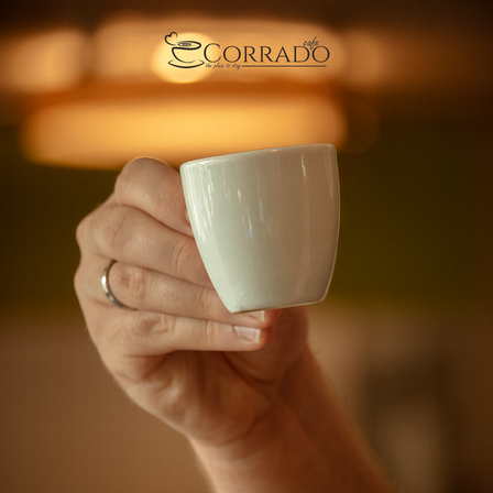 Eine Hand hält eine weiße Kaffeetasse vor einem Hintergrund mit weichem, gelbem Licht.