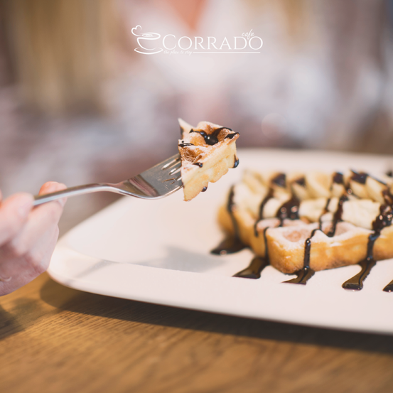 Nahaufnahme der Hand einer Person, die einen Gabel mit einem Stück Schokoladenwaffe von Corrado Cafe hält.