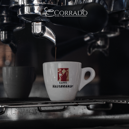 Kaffee wird aus einer Kaffeemaschine in eine weiße Tasse mit rotem Logo gegossen.