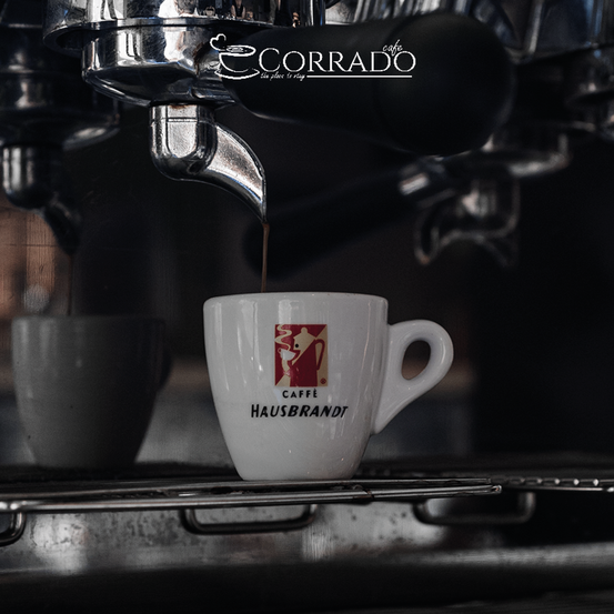 Kaffee wird aus einer Kaffeemaschine in eine weiße Tasse mit rotem Logo gegossen.