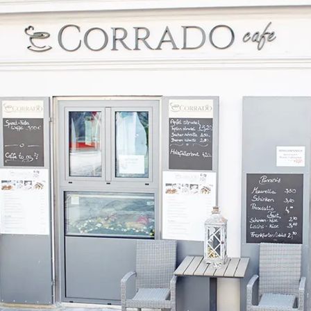 Die Vorderseite eines Restaurants namens Corrado Cafe mit Speisekarten, Stühlen und einer Laterne auf dem Tisch.