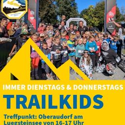Eine Gruppe von Kindern und Erwachsenen posiert für ein Foto in einem Waldgebiet und trägt verschiedene Nummern auf ihren Trikots. Das Bild zeigt die Worte 'TRAIL KIDS' und 'IMMER DIENSTAG & DONNERSTAGS'. Der Ort ist Oberaudorf am Luegsteinsee.