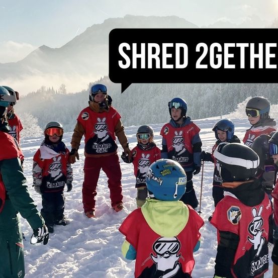Snowboarder in roten Jacken mit einer weißen Comic-Figur, stehen im Schnee mit Bergen im Hintergrund. Ein Textballon darüber lautet 'SHRED 2GETHER.'