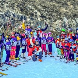 Eine Gruppe von Kindern und Erwachsenen posiert für ein Foto auf verschneiten Hängen mit Skiausrüstung, einige mit Helmen, vor einem felsigen Berg.