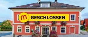 Ein rotes Gebäude mit einem gelben Schild über dem Eingang steht 'Geschlossen'. Das Gebäude hat weiße Fenster und Türen, und Blumen hängen an den Fenstern.