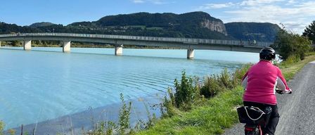 Ein Radfahrer fährt auf einem Schotterweg in der Nähe eines Sees mit einer Brücke im Hintergrund.