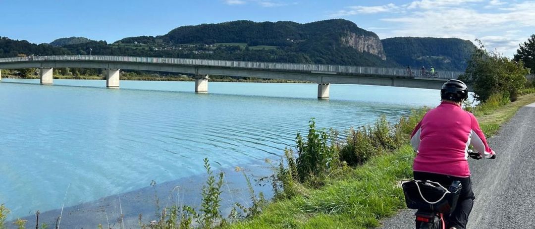 Ein Radfahrer fährt auf einem Schotterweg in der Nähe eines Sees mit einer Brücke im Hintergrund.
