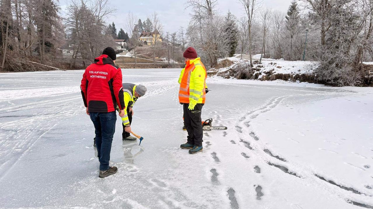Drei Personen in Schutzkleidung stehen auf einem zugefrorenen See. Einer hält eine Kettensäge und ein anderer einen Axt. Bäume umgeben das Gebiet.