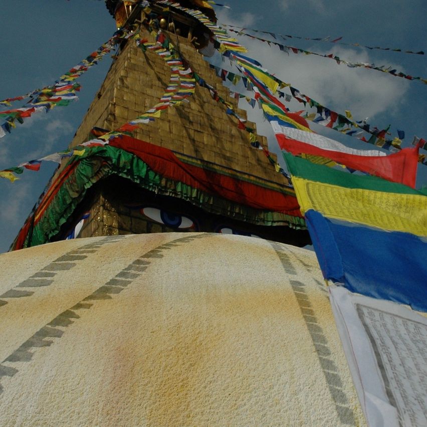 Ein lebendiger Nahaufnahme eines buddhistischen Tempels mit vielen bunten Fahnen und einem großen Augendesign an seiner Fassade.