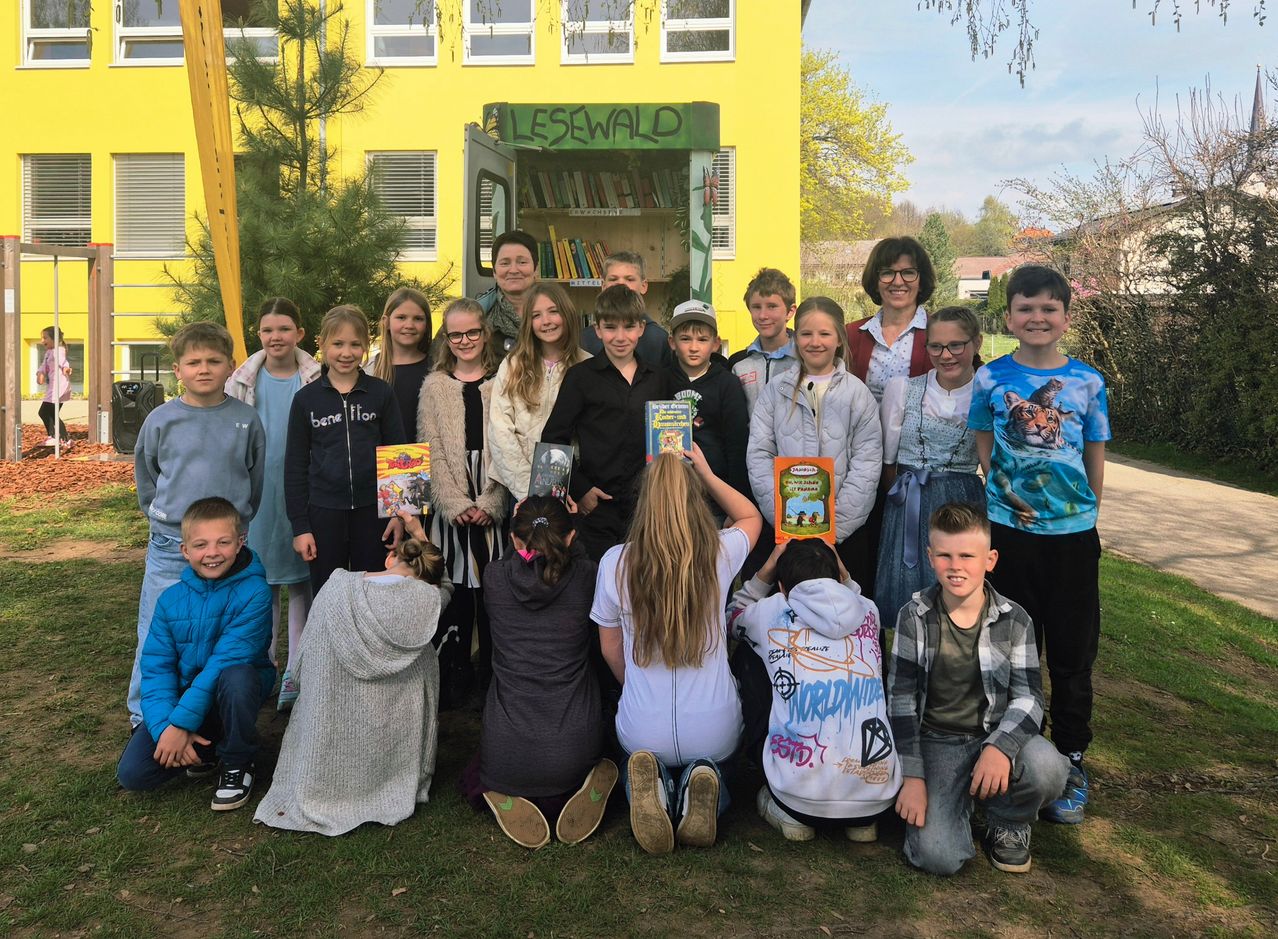 Eine Gruppe von Kindern und zwei Erwachsenen posiert für ein Foto vor einer kleinen, gelben Bibliothek.