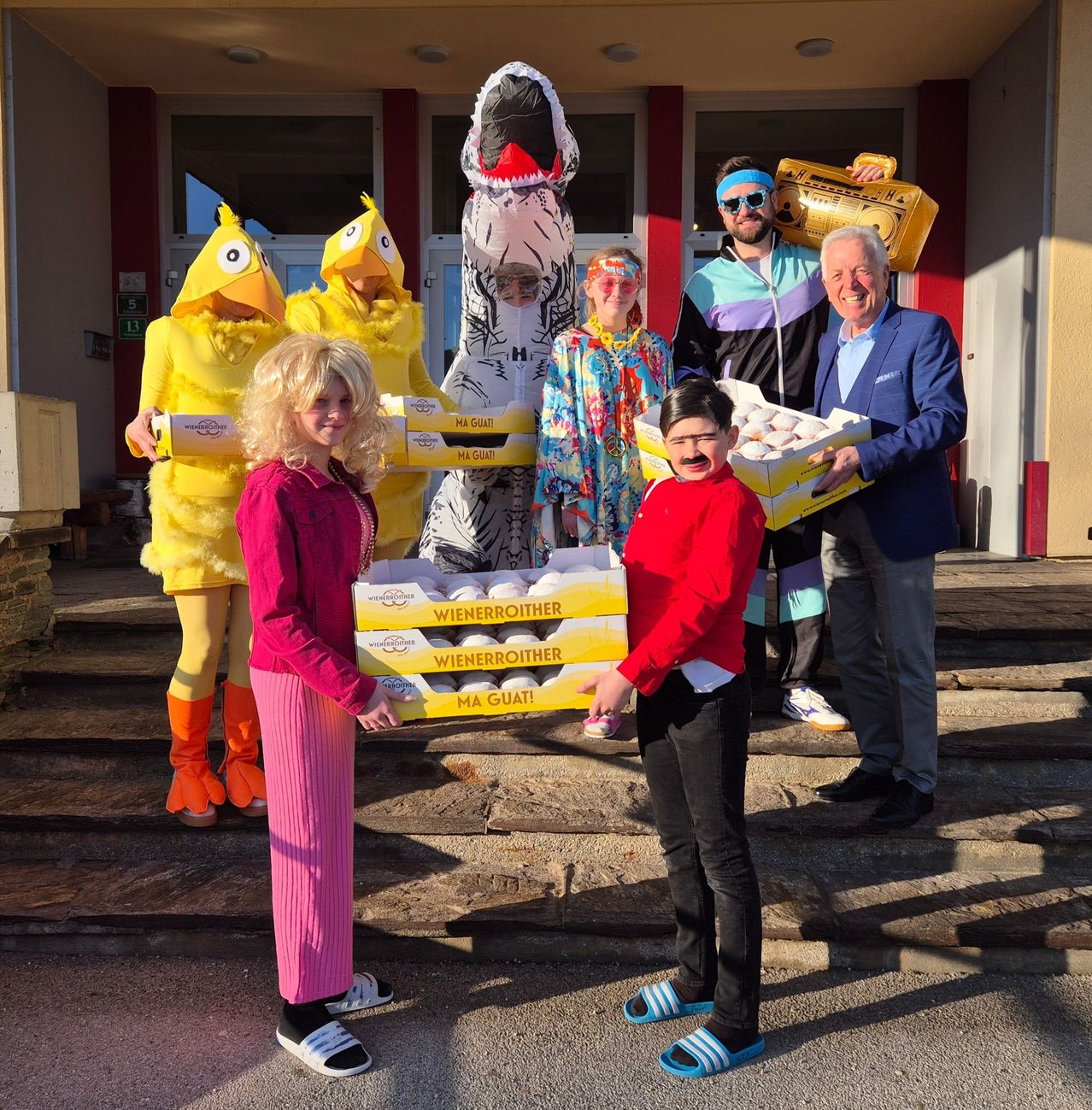 Eine Gruppe von Menschen in Kostümen, darunter ein Dinosaurier, steht auf einer Treppe und hält Eierkartons in der Hand, mit zwei Kindern vorne.