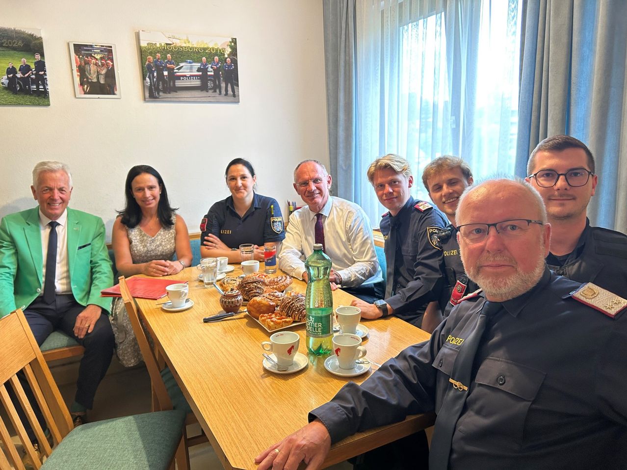 Eine Gruppe von Menschen, einschließlich Polizeibeamten, sitzt um einen Tisch mit Essen und Getränken. Sie lächeln und scheinen in einer Besprechung zu sein.